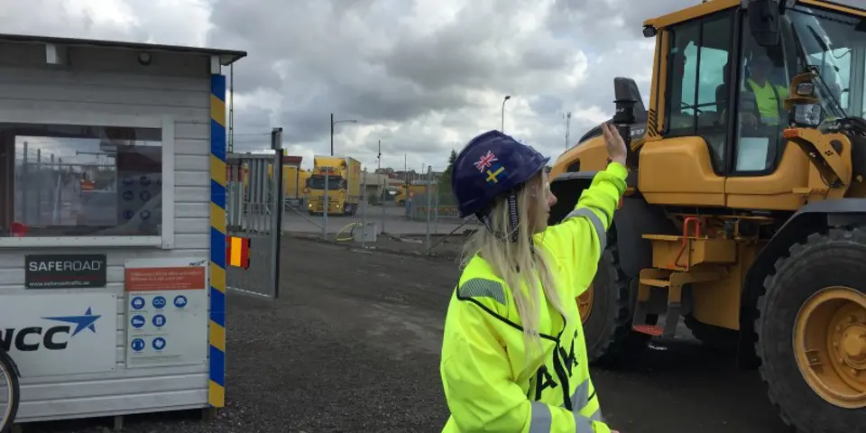 Vakt vinkar åt lastmaskinförare hon just släppt in på arbetsområdet